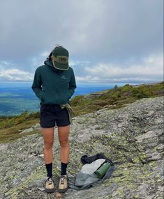 a woman standing on top of a mountain next to a backpack