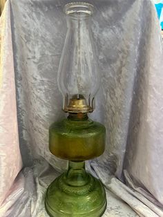 a green glass lamp sitting on top of a white tablecloth covered table next to a curtain