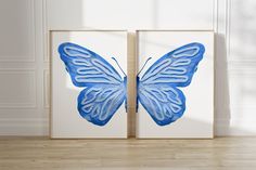 two blue butterfly paintings on white canvases in an empty room with wood flooring