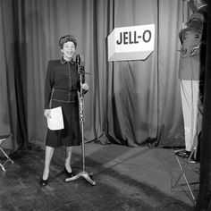 a black and white photo of a woman standing in front of a jello sign