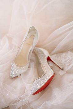 a pair of white shoes with red soles on top of a wedding dress sheet