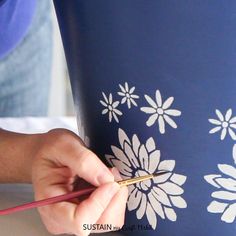 a person is painting a flowered vase with gold paint and a red pencil in their hand