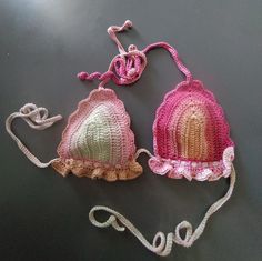 two crocheted hats are sitting on a black surface, one is pink and the other is green