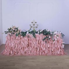 the table is covered with pink ruffles and greenery as well as flowers