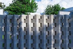 a concrete wall with holes in the middle and trees behind it on a sunny day