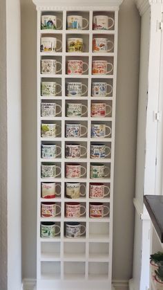 a white bookcase filled with coffee mugs in a room next to a wall