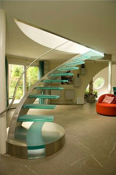 a spiral staircase in a modern home with glass railings on each side and an orange chair at the bottom