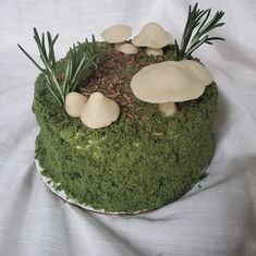 a cake with moss and mushrooms on it sitting on a white cloth covered tablecloth