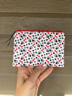 a hand holding up a white and red dog paw print pouch with black dots on it