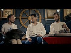 three men sitting on a couch talking to each other in front of a wall clock