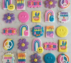 many decorated cookies are arranged on a marble countertop with peace, flowers, and rainbows