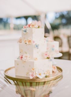 a three tiered cake with flowers on it sitting on top of a glass table