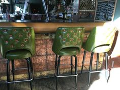 three green leather bar stools sitting in front of a counter