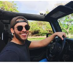 a man wearing sunglasses sitting in the driver's seat of a car