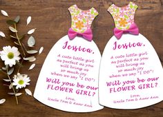 two bridesmaid dresses with pink bows and flowers next to them on a wooden table