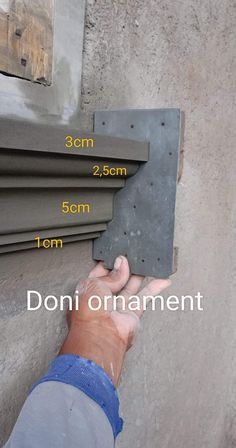 a hand is holding up a piece of cement to the side of a building with measurements