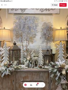 a christmas scene with deer, pine cones and evergreens on a dresser in front of a large painting