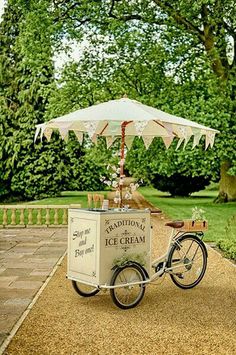 an ice cream cart in the middle of a park with a white umbrella over it