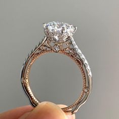 someone is holding an engagement ring that has been set in gold and diamond band, with the center stone surrounded by smaller diamonds