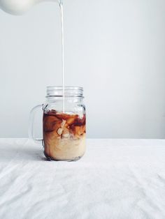 a person pouring liquid into a jar filled with food items on a white tablecloth