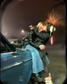 two people sitting on the hood of a car, one with her hair blowing in the wind