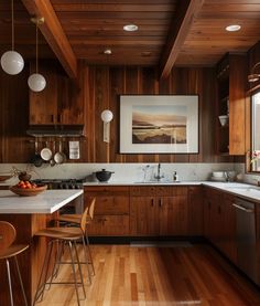 a kitchen with wood paneling and white counter tops, wooden flooring and hanging lights