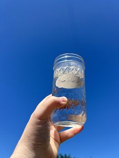 a person holding up a glass with water in it on a clear blue sky day