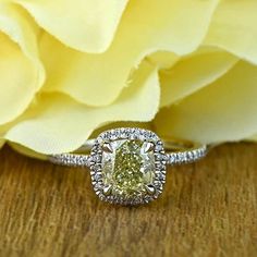 a yellow diamond ring sitting on top of a wooden table next to a white rose