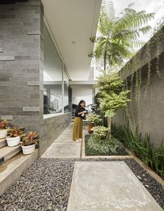 a woman standing in front of a building next to plants and rocks on the ground