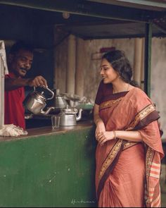 a woman standing next to a man in front of a green wall with pots and pans on it