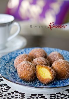 powdered sugar covered donuts on a blue and white plate next to a cup