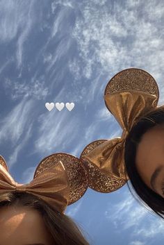 two girls wearing gold minnie ears with hearts in the sky behind them and one girl has her hair pulled back