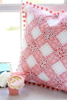 a pink and white pillow sitting on top of a table next to a vase with flowers