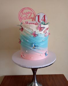 a birthday cake with butterflies on it sitting on top of a wooden table in front of a white wall