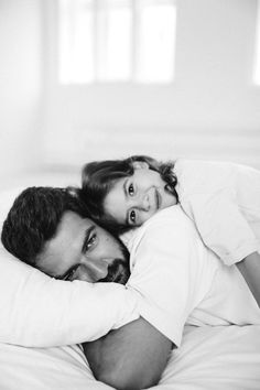 a man and woman laying on top of each other in bed with white linens