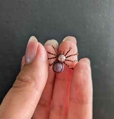 a woman's hand holding a tiny spider with a pearl bead on it