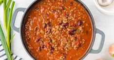 a pot filled with chili and beans next to green onions