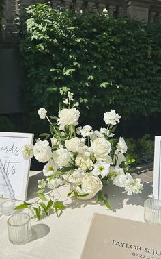 white flowers in vases sitting on top of a table next to cards and candles