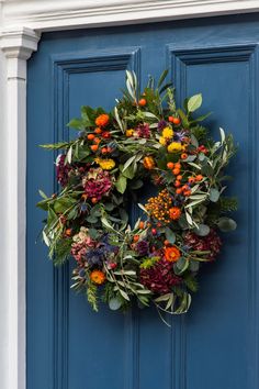 a blue door with a wreath hanging on it's side and flowers in the middle