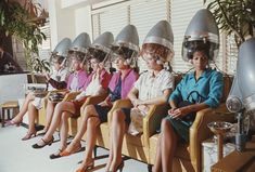 several women sitting in chairs with hair dryers on their heads