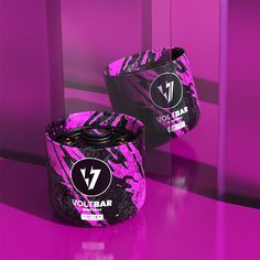 two black and purple containers sitting on top of a counter next to each other in front of a pink wall