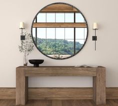 a round mirror on the wall next to a wooden table with a vase and potted plant