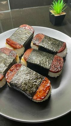 several pieces of sushi on a white plate next to a green potted plant