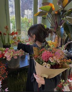 a woman holding a bouquet of flowers in front of a table with potted plants