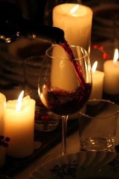 wine being poured into a glass in front of candles