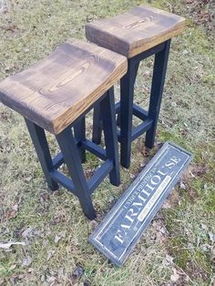 two wooden stools sitting on top of a grass covered field next to a sign