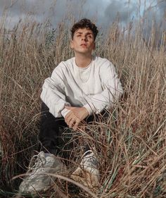 a young man sitting in tall grass with his hands on his knees and eyes closed