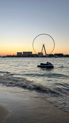 the ferris wheel is in the distance over the water at sunset or dawn on the beach