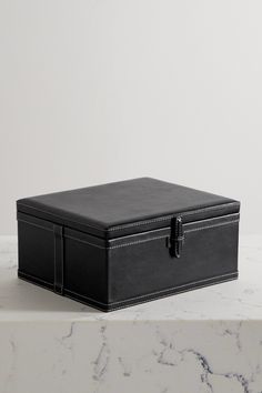 a black leather box sitting on top of a white marble countertop next to a wall