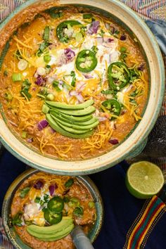 two bowls filled with chili, cheese and avocado on top of a table